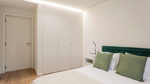 A bedroom with a bed, green and white pillows, a nightstand with a lamp, and a white wardrobe.