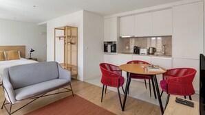 A modern hotel room with a bed, a sofa, a dining table with red chairs, a kitchen area, and a TV. - The Lisbon Urban Nook Studio (Lisbon)