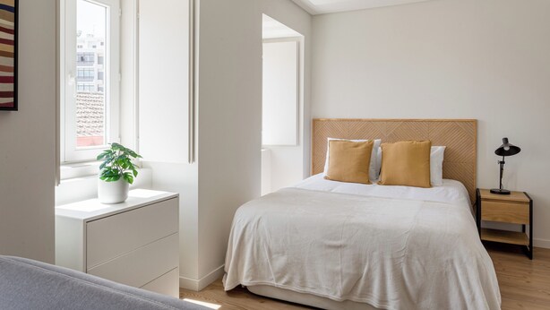 A bedroom with a bed, bedside table, lamp, and a window with a plant. - The Lisbon Urban Nook Studio (Lisbon)