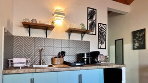 Uma cozinha com design moderno, apresentando um painel de azulejos em padrão herringbone, uma cafeteira embutida e uma prateleira de madeira com utensílios de cozinha.