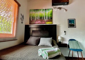 Un dormitorio con cama, un cuadro, una silla y una mesita de noche.