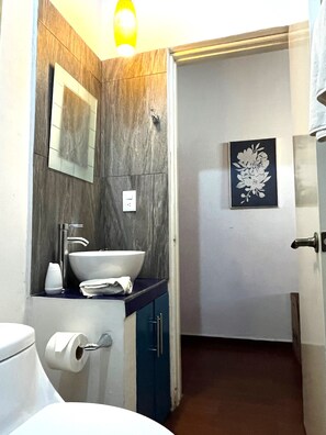 Un baño con tocador de madera, lavamanos, espejo, toalla y retrete.
