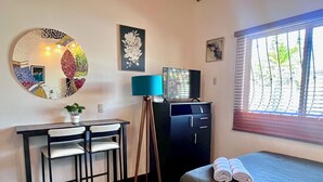 Quarto com cama, escrivaninha, cadeiras, televisão, abajur e obras de arte nas paredes.