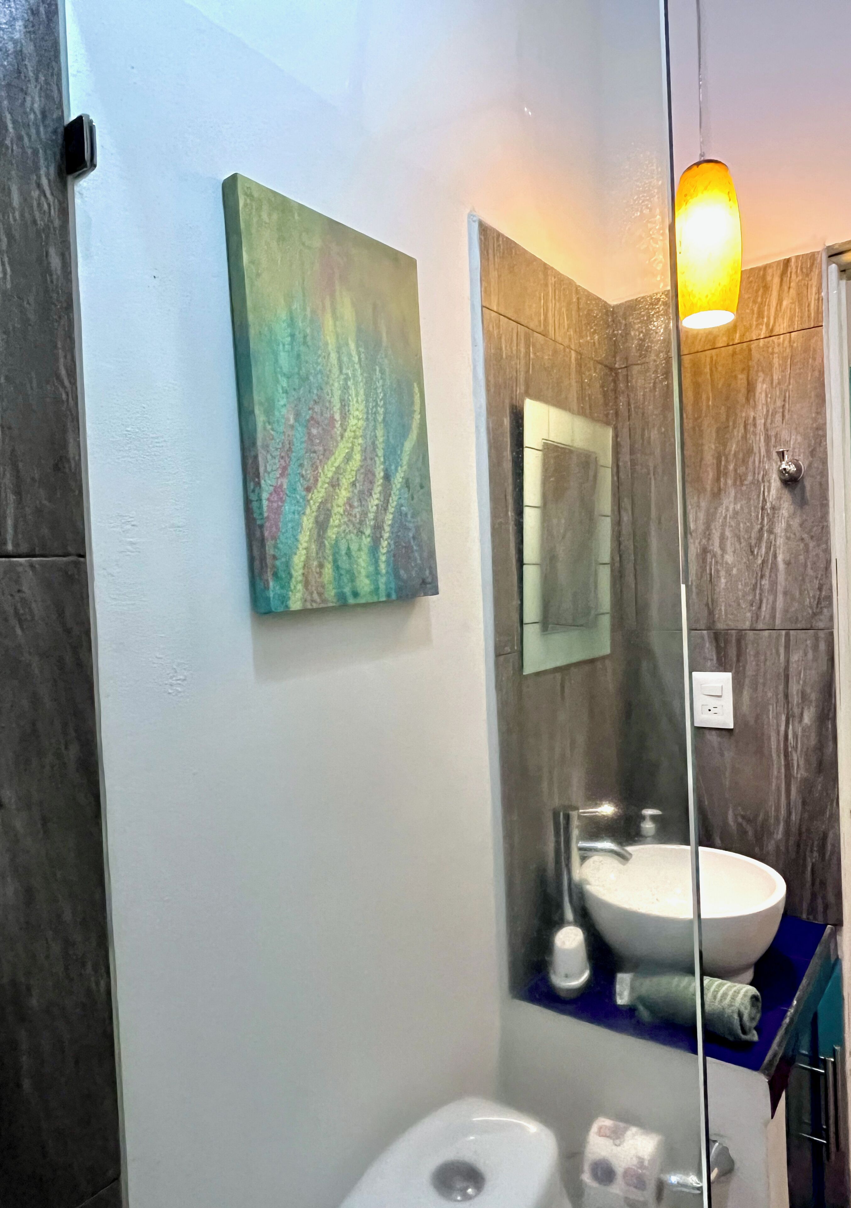 Un baño moderno con cabina de ducha de vidrio, un lavabo blanco y un cuadro abstracto colorido en la pared.