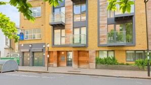 A modern multi-story building with a mix of brick and wood paneling, large windows, and a green door. - Still Life Farringdon (London)