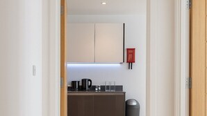A hallway leading to a modern kitchen with wooden flooring and a trash bin. - Still Life Farringdon (London)