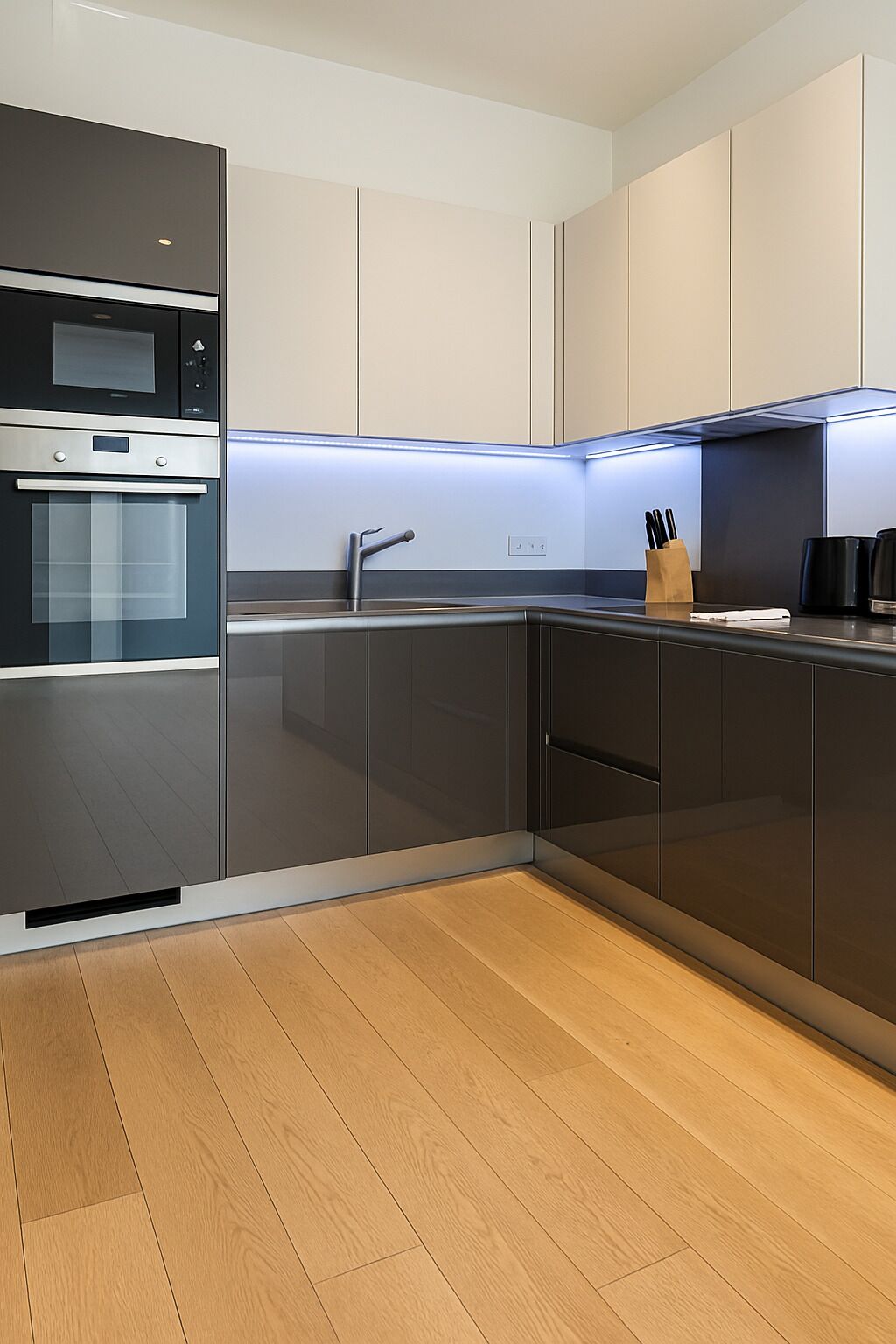 A modern kitchen with a built-in oven, a stainless steel sink, and a wooden floor.
