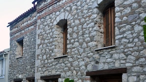 A stone building with wooden shutters, a large potted plant, and a bench. - Limni Stone Apartment (Mantoudi-Limni-Agia Anna)