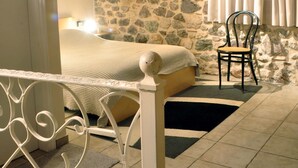A bedroom with a stone wall, a bed, a chair, and a window with curtains. - Limni Stone Apartment (Mantoudi-Limni-Agia Anna)