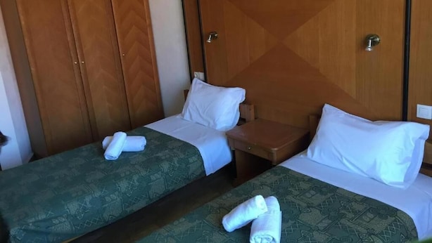 Una habitación de hotel con dos camas individuales, un armario de madera y una mesita de noche pequeña.