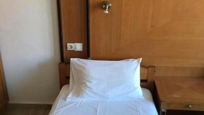 Una habitación de hotel con cabecera de madera, cama con sábanas blancas y colcha estampada verde.