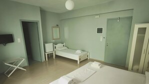 A hotel room with a large bed, a smaller bed, a desk, a chair, a TV, and a door. - Valente Perlia Rooms (Poros)