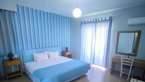 A bedroom with a large bed, a desk, a chair, a nightstand, and a mirror. - Valente Perlia Rooms (Poros)