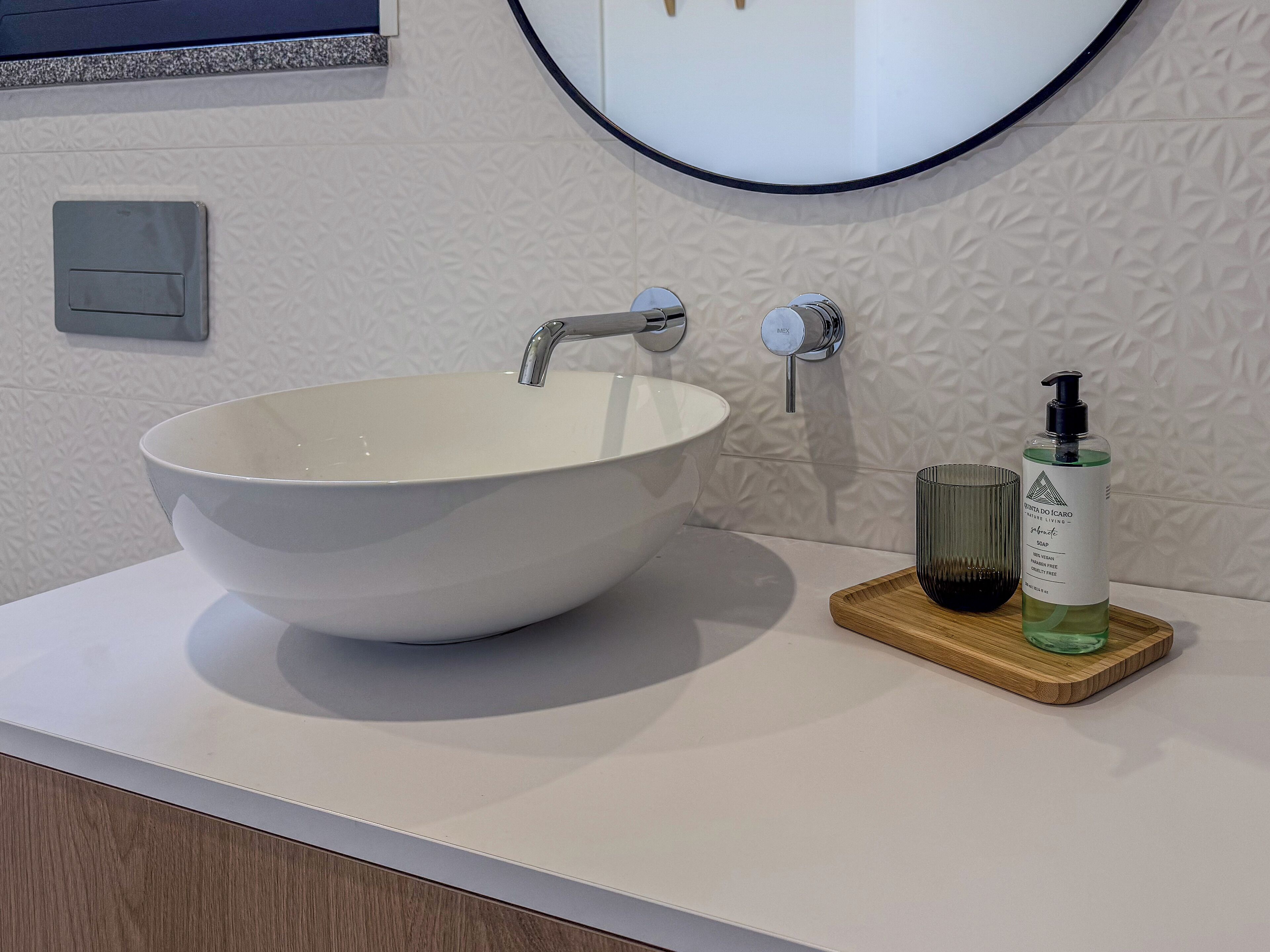 Un bagno con un lavabo a incasso bianco, uno specchio e un erogatore di sapone su un vassoio di legno.