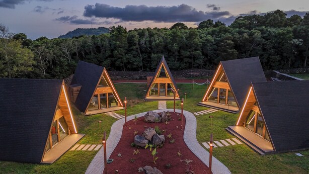 A row of modern, triangular A-frame cabins with glass doors and windows, surrounded by a landscaped garden with a central pathway.