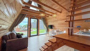 A modern interior with a wooden sloped ceiling, a sofa, a dining table with chairs, and a staircase.