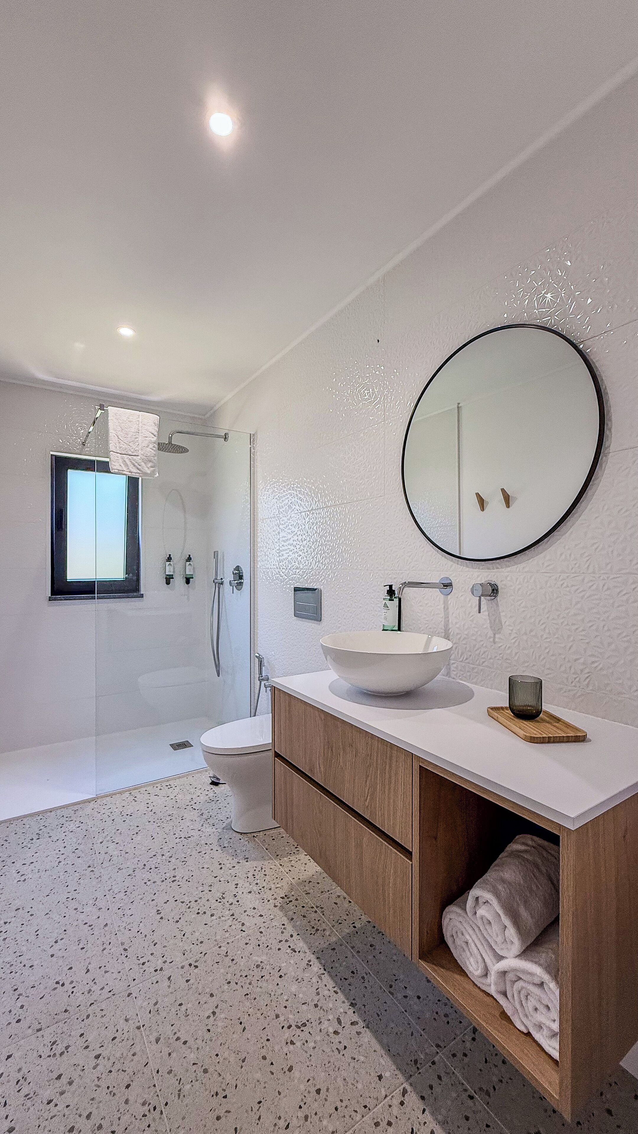 Un baño moderno con una bañera independiente, un espejo redondo y un lavamanos grande.