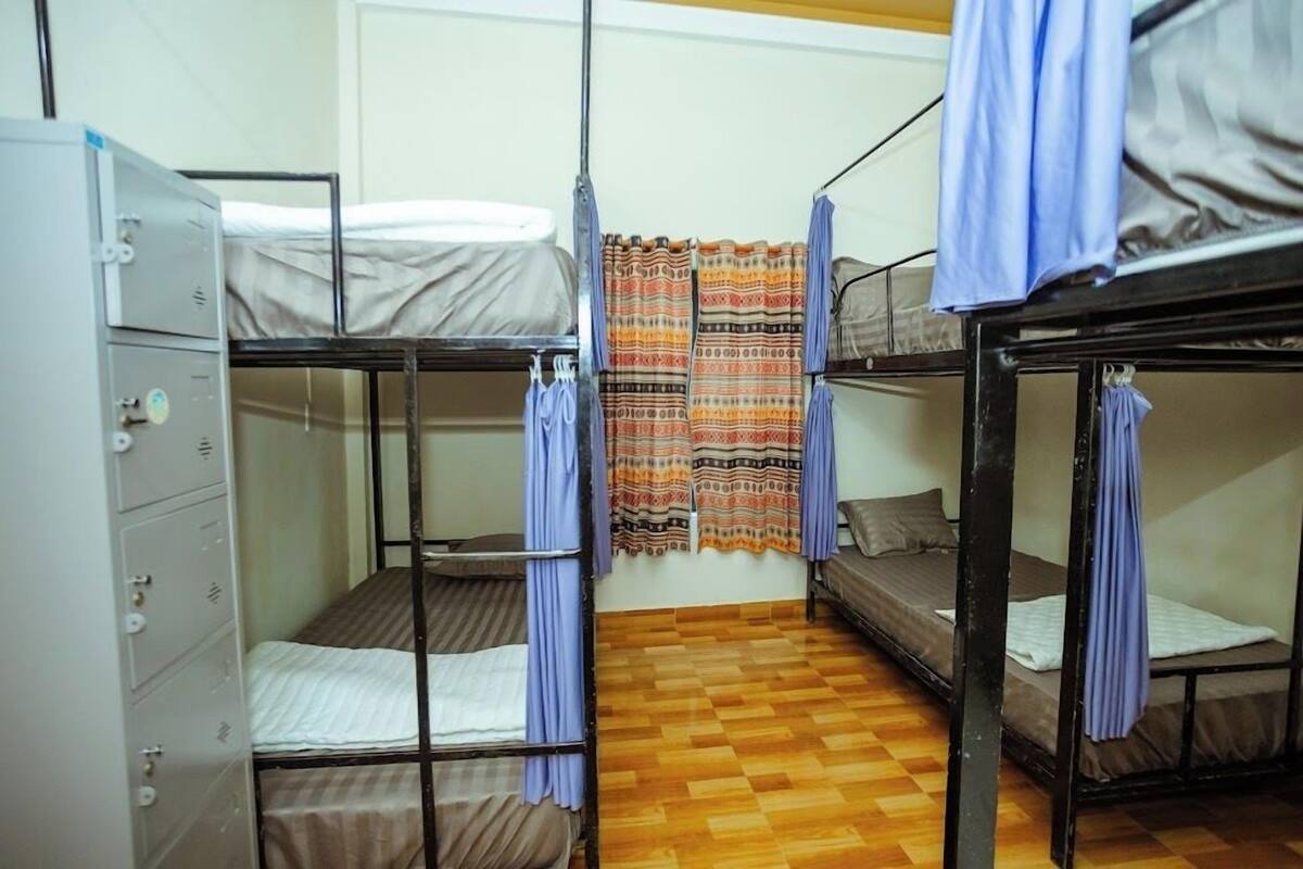 A dormitory room with bunk beds, a wardrobe, and a patterned curtain.