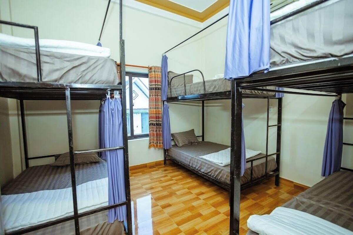 A dormitory room with bunk beds, wooden flooring, and curtains.