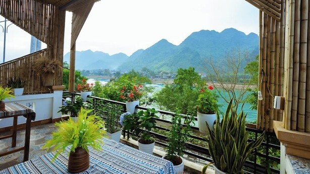 A balcony with potted plants, a patterned rug, and a view of mountains and water. - Phong Nha Homie Home (Phong Nha)