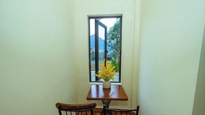 A small dining area with a table and chairs, a window with a view of greenery and buildings, and a vase with flowers on the table. - Phong Nha Homie Home (Phong Nha)
