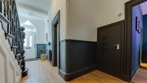 A hallway with a wooden floor, a black door, and a staircase with dark balusters. - The Rockfield By Serene Stays (Anfield)