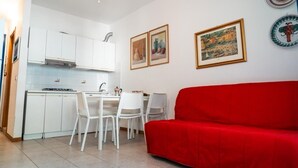 Ein kleiner Wohnraum mit Küchenzeile, weißen Schränken, einem roten Sofa und gerahmten Bildern an den Wänden.