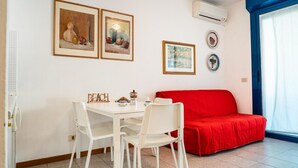 Ein Zimmer mit einem weißen Tisch und Stühlen, einem roten Sofa und drei gerahmten Kunstwerken an der Wand.