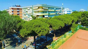 A multi-story building with balconies, surrounded by trees and a tennis court.