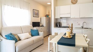A modern kitchen with white cabinets, a dining table with chairs, a refrigerator, and a clock on the wall.