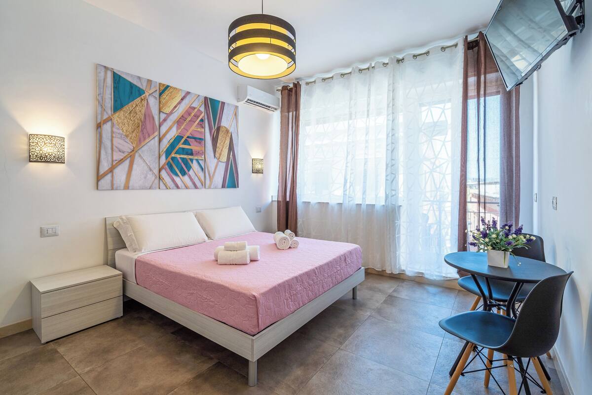A modern bedroom with a bed, bedside table, and a dining area with chairs and a table.