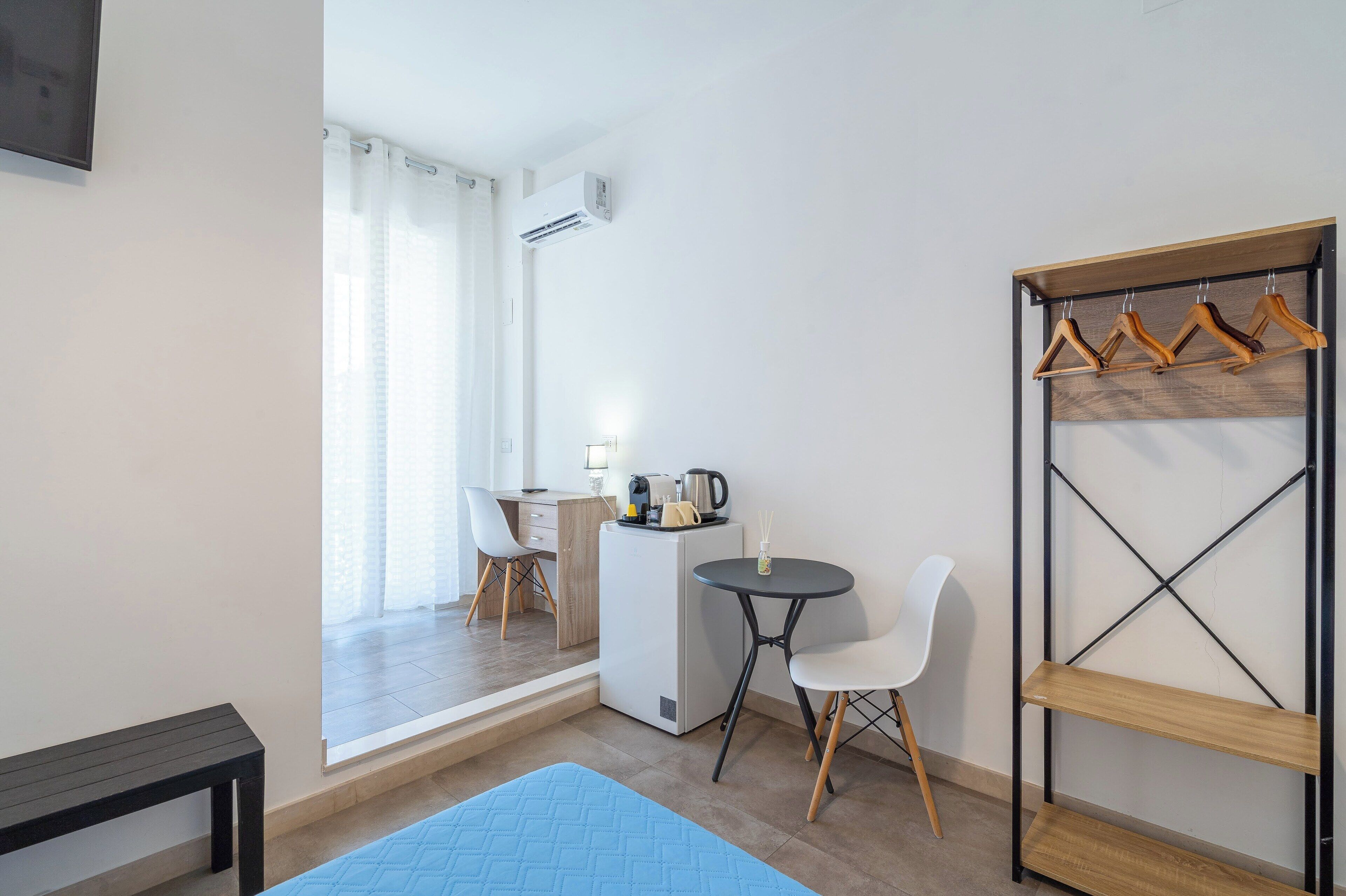 Una camera compatta con un letto, un piccolo tavolo con sedie, una scrivania e un armadio con grucce in legno.