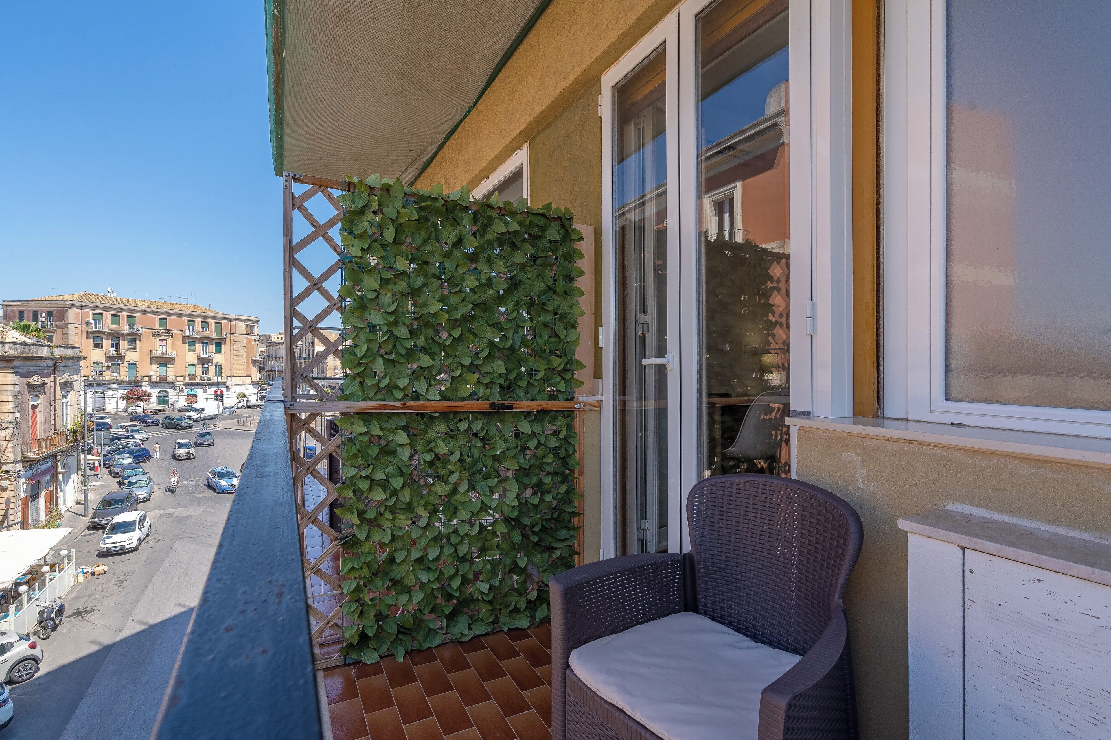 A balcony with a wicker chair and a green leafy wall.