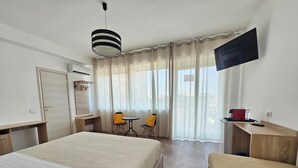 Habitación de hotel con dos camas, un escritorio, una silla, un televisor y un balcón con cortinas.