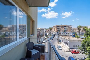 A balcony with wicker furniture overlooking a busy street with cars and buildings. - Agorà (Syracuse)