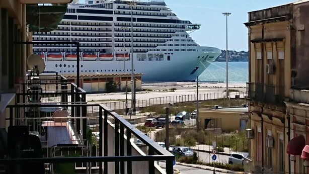 Un gran crucero amarrado en un puerto, con vista al mar y un edificio con balcones.