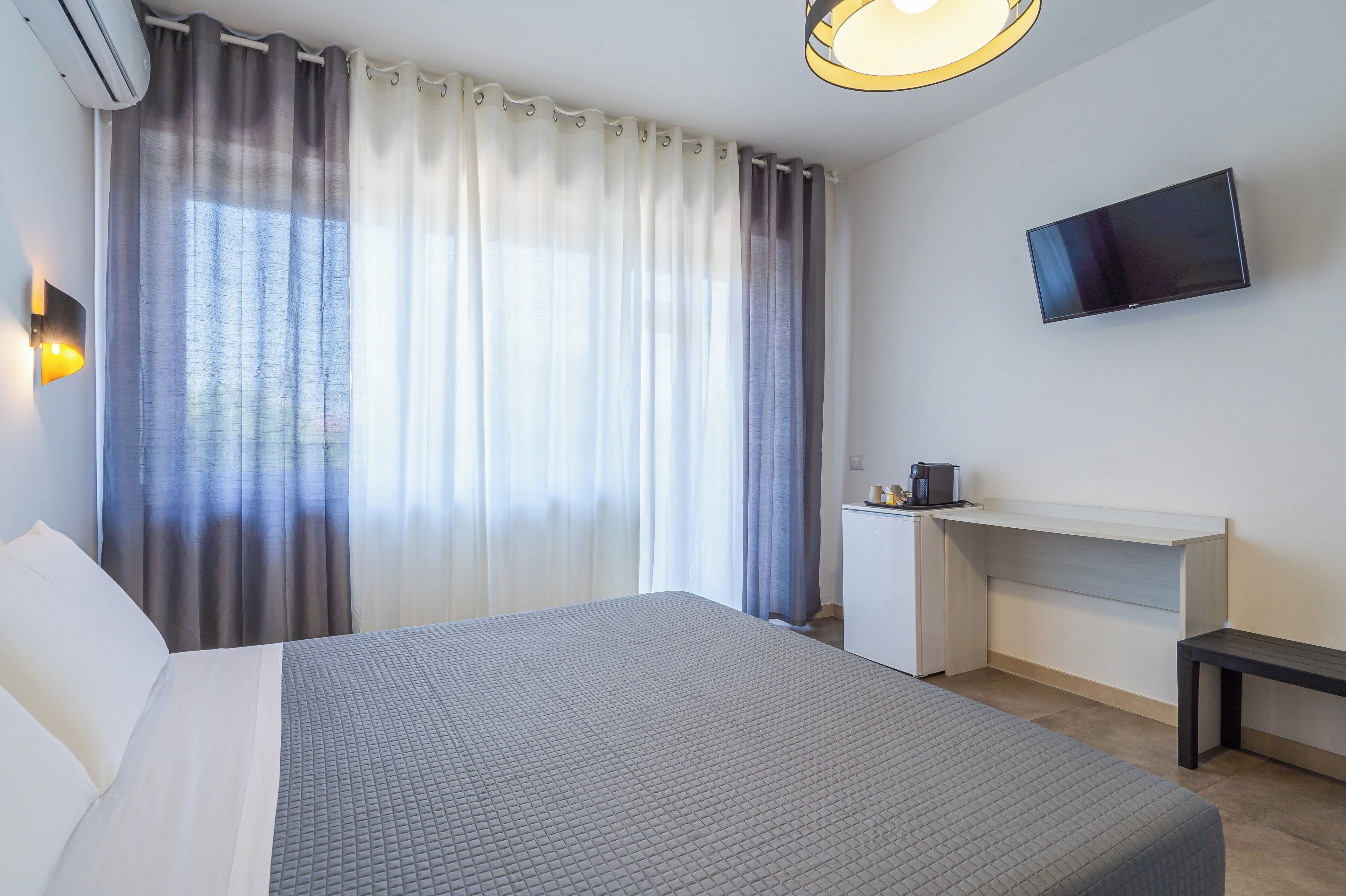 Une chambre d’hôtel avec un lit, un bureau, une télévision et une fenêtre avec des rideaux.