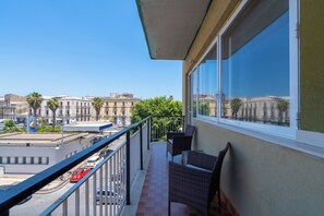 A balcony with wicker furniture, a view of the cityscape, and a clear blue sky. - Agorà (Syracuse)