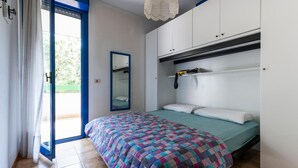 Un dormitorio con cama, armario, espejo y puerta que da a un espacio exterior.