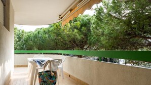 Un balcón con una mesa y sillas, una bolsa colgada y vistas a pinos.