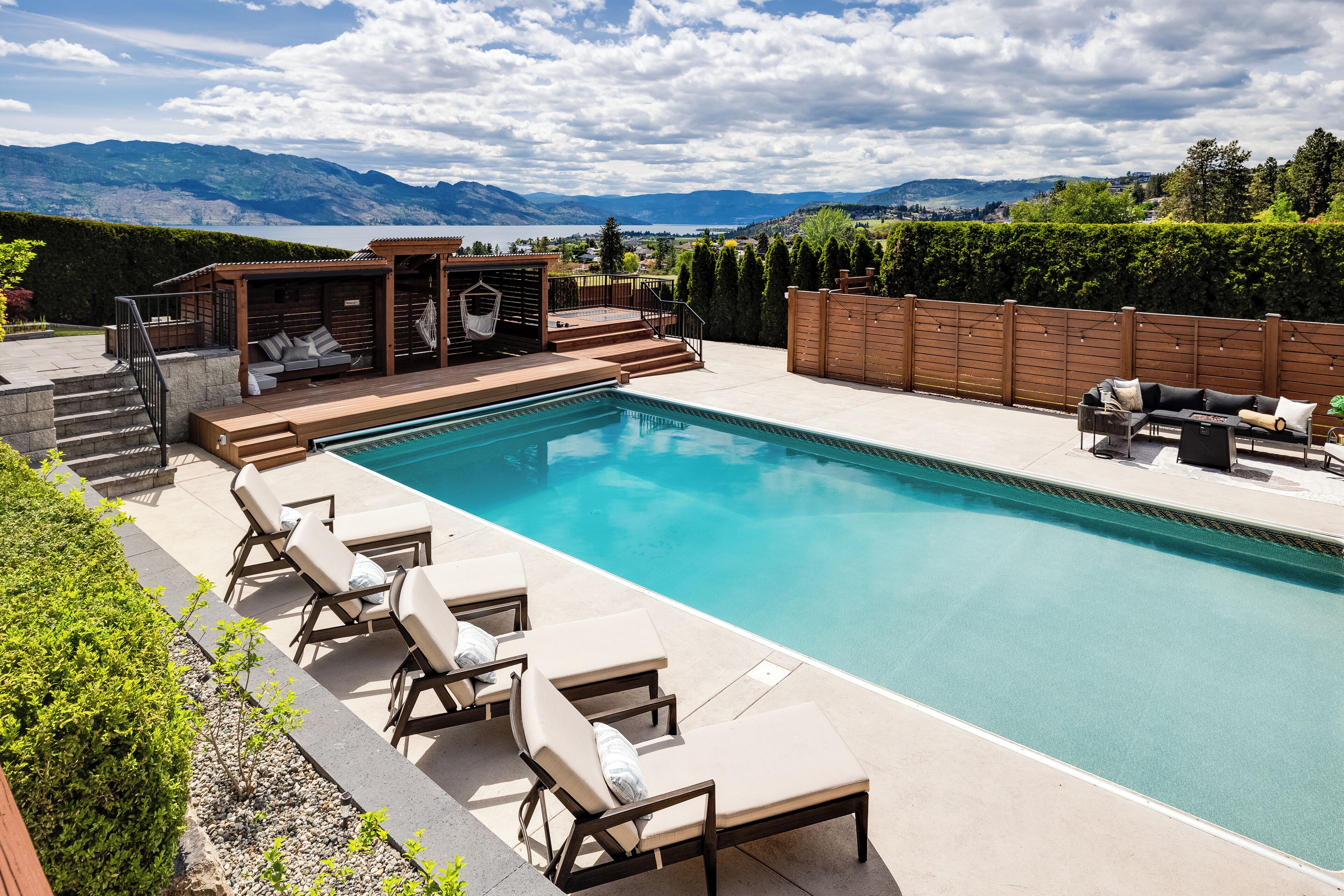 Une piscine avec des chaises longues, une terrasse en bois et une vue sur les montagnes.