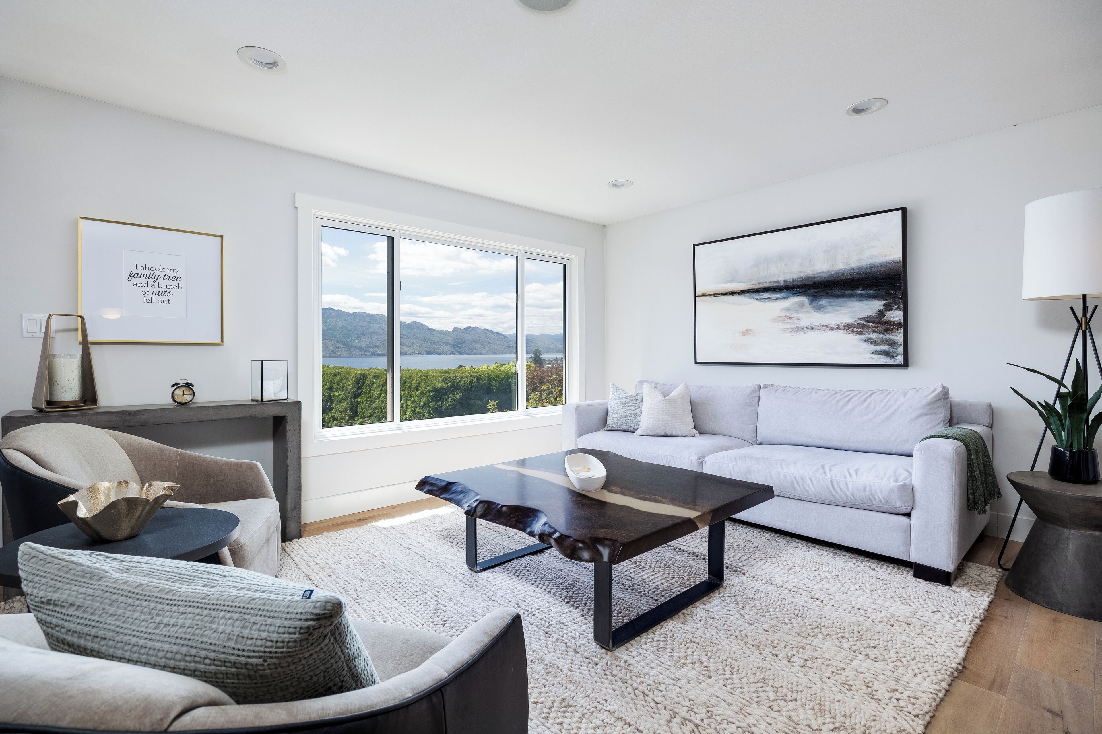A modern living room with a sofa, armchairs, a coffee table, and a view of mountains and water through large windows.