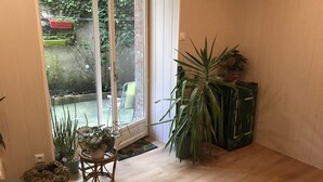 Une pièce dotée d’un plancher en bois, d’une porte-fenêtre coulissante donnant sur un jardin et de plusieurs plantes en pot.