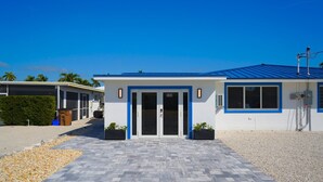 A modern building with a blue roof and white walls, featuring a numbered entrance door and a paved walkway. - H's Hideaway - Key Colony Beach (Marathon)