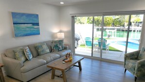 A living room with a sofa, a coffee table, and a painting of a beach scene. - H's Hideaway - Key Colony Beach (Marathon)