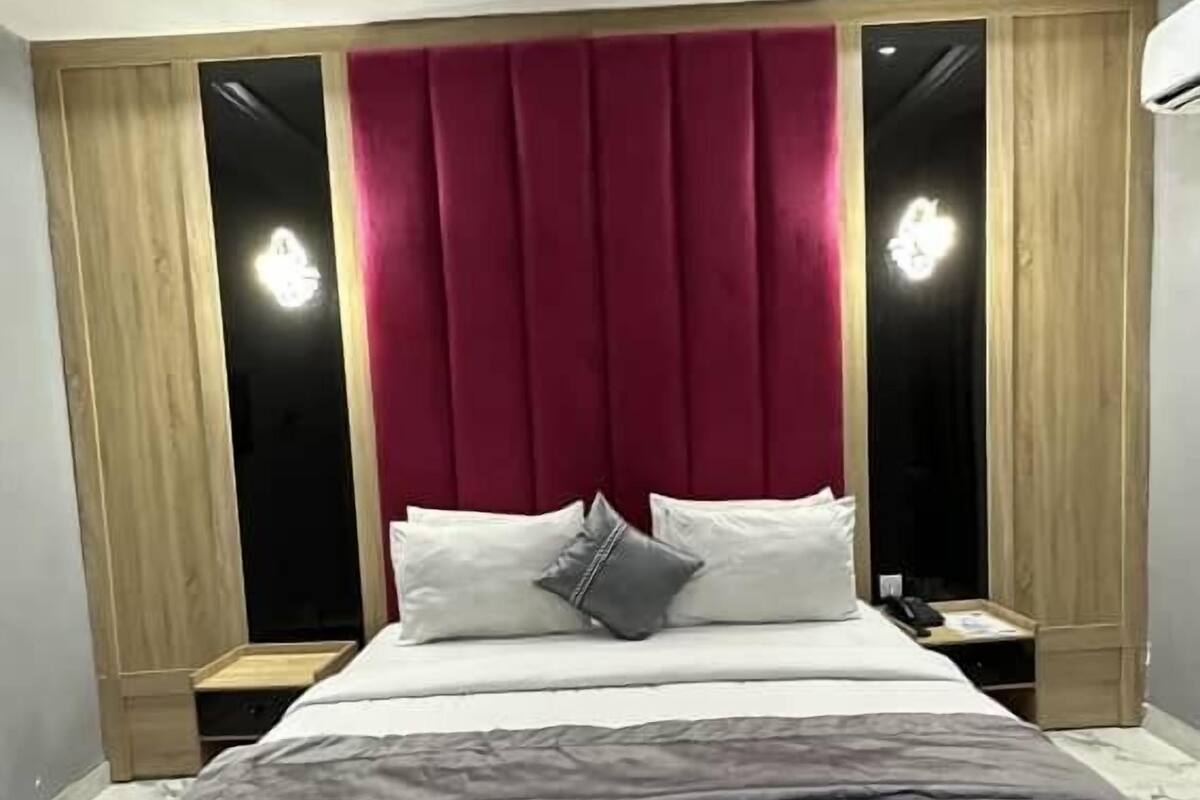 A modern bedroom with a large bed, wooden paneling, and a red headboard.