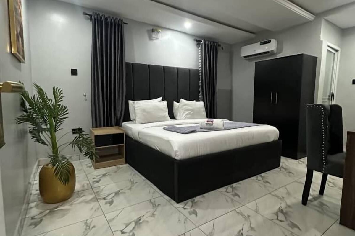 A modern bedroom with a large bed, a wardrobe, a desk, and a potted plant.