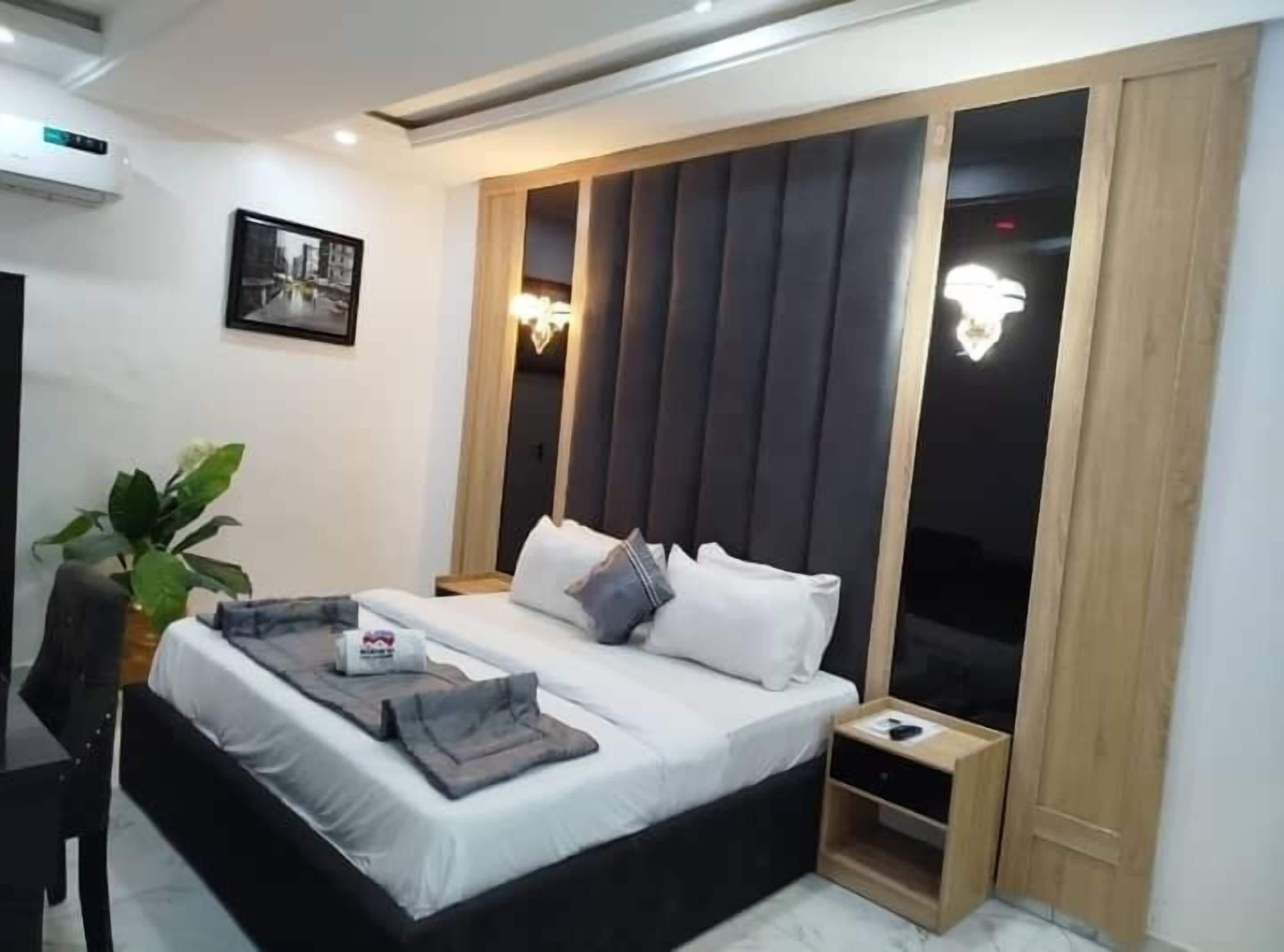 A modern bedroom with a large bed, bedside tables, a desk, and a potted plant.