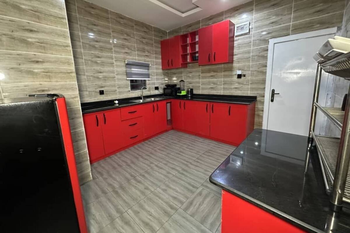 A kitchen with red cabinets, a black countertop, and a tiled backsplash.