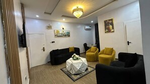 A modern living room with a chandelier, a black and yellow sofa set, a coffee table with a floral centerpiece, and artwork on the walls. - mountaintop suite and apartment (Lagos)